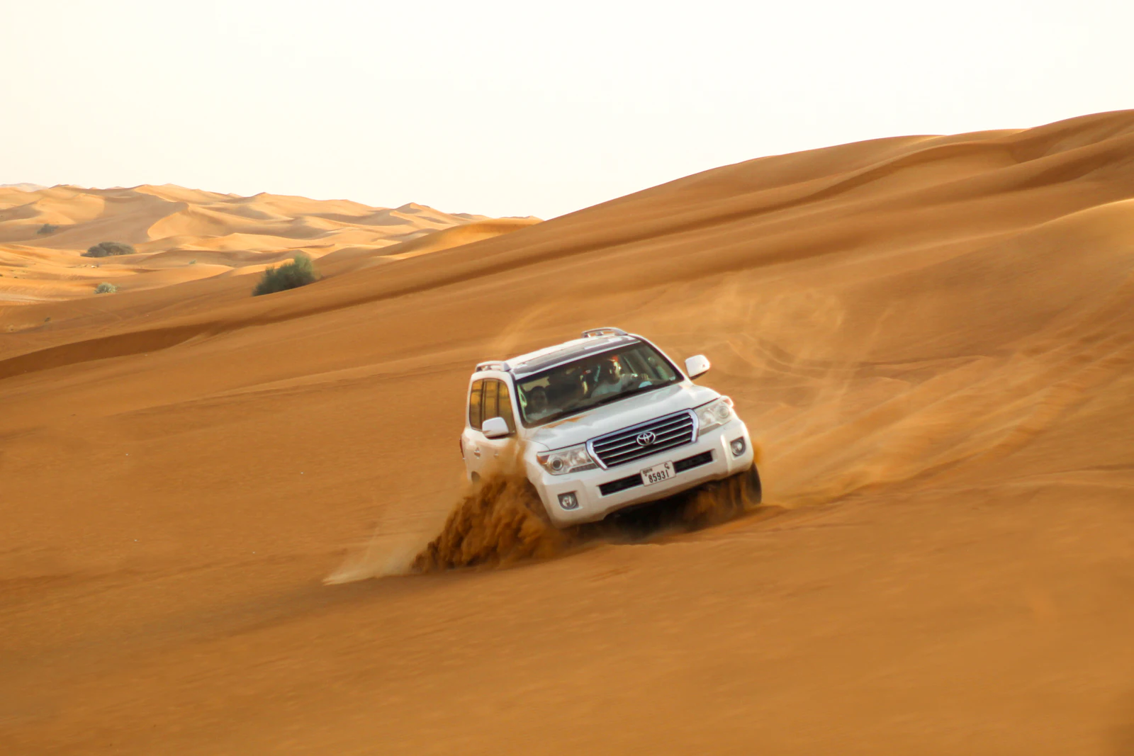 suzu abroad dubai desert safari dune drive White Land Cruiser driving over red sand dunes on a desert safari near Dubai